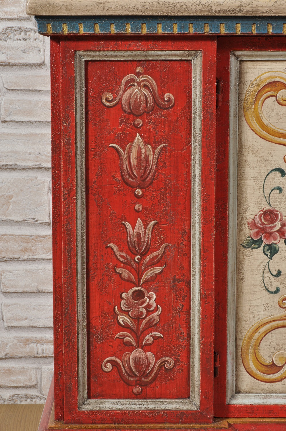 lavorazioni artigianali su misura della credenza cassapanca porta tv tirolese decorata con pilastri dalle tonalità vivaci del rosso e giallo con pitture di fiori e barocchi eseguiti a mano